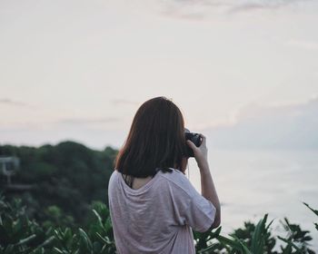 Rear view of woman photographing calm lake