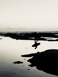 Silhouette man on rock in sea against clear sky