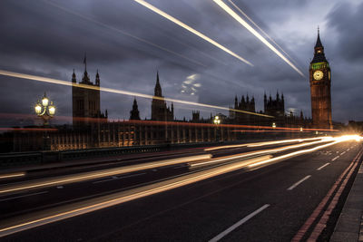 Light trails on westminster bridge by big ben against cloudy sky at dusk