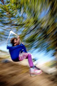 Blurred motion of little girl swinging against tree