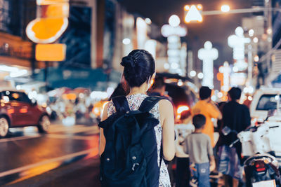 Rear view of woman standing on illuminated city street