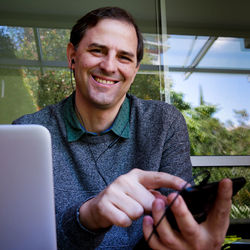 Portrait of smiling man using mobile phone against glass building 