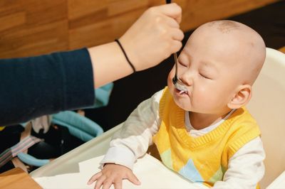 Cropped hand of woman feeding baby sitting on high chair