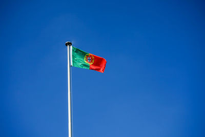 Low angle view of portuguese flag waving against clear blue sky