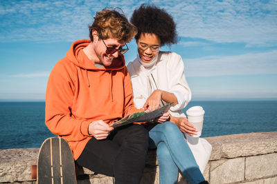 Friends sitting on sea shore against sky