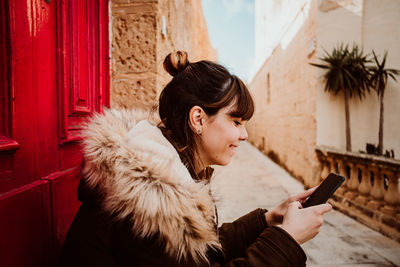 Close-up of woman using smart phone while sitting by door