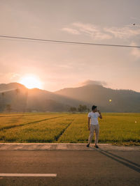 Rear view of man standing on mountain against sky during sunset