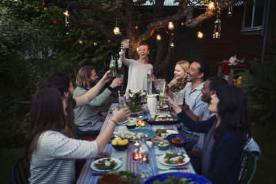 Happy woman toasting drink to friends at dining table while enjoying outdoor dinner party