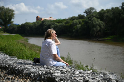 Side view of woman sitting on rock by lake