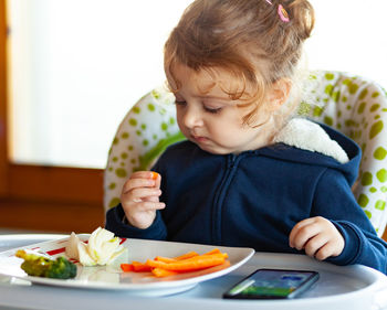 Cute girl eating meal on high chair at home