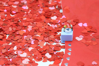 Close-up of hole puncher with figurines on red hear shapes at table