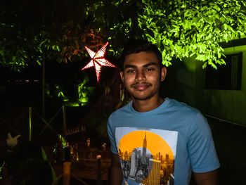 Portrait of young man standing against illuminated wall at night