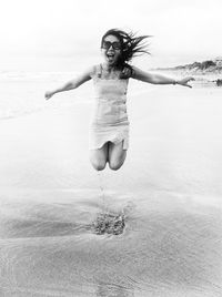 Portrait of young woman jumping on shore at beach