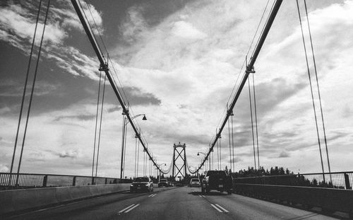 Road by suspension bridge against sky