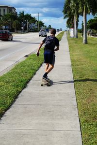Rear view of boy skateboarding on footpath by street