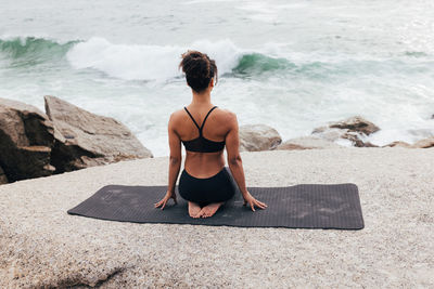 Rear view of woman sitting on rock at beach