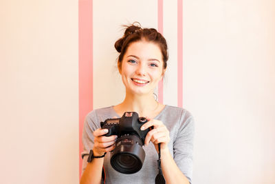 Portrait of happy beautiful woman holding slr camera against wall