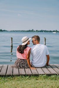 Rear view of couple sitting on shore against sky