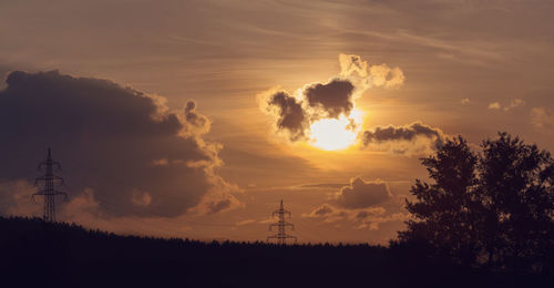 Silhouette trees and electricity pylon against sky during sunset