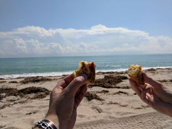 Cropped hands holding food at beach against sky