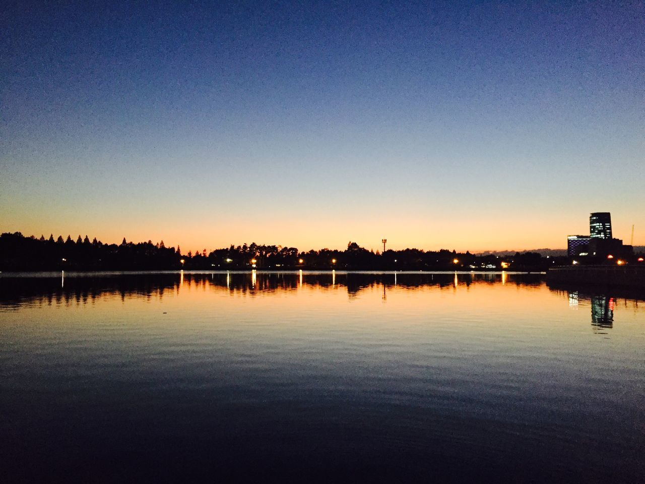 water, sunset, clear sky, illuminated, copy space, reflection, waterfront, built structure, silhouette, architecture, tranquil scene, tranquility, night, scenics, building exterior, dusk, river, orange color, lake, blue