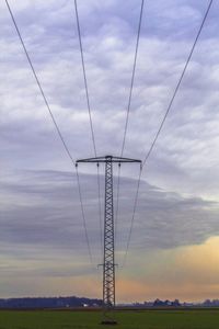 Low angle view of electricity pylon on field against cloudy sky