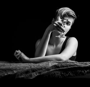 Young woman sitting at the table against black background looking at the broken glass