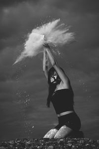 Young woman splashing powder against sky