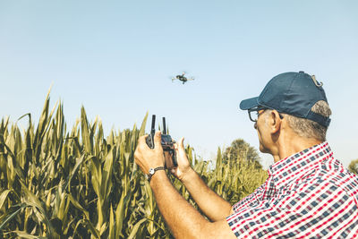 Man flying drone while standing amidst plants against clear sky