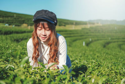 Young woman looking at plant while standing on agricultural field
