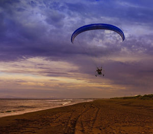 Silhouette of powered paraglider soaring flight over the sea against sunset sky