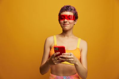 Portrait of young woman holding mobile phone against yellow background