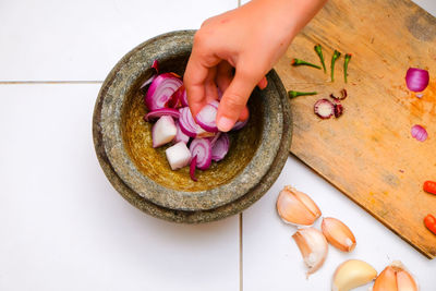 Cropped hand of woman putting onions in mortar and pestle
