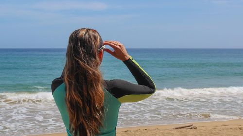 Rear view of woman standing on beach against sky