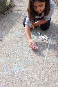 High angle of girl writing with chalk on footpath