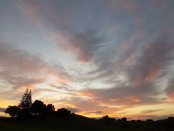 Silhouette trees on landscape against dramatic sky