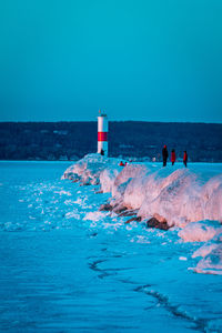 People on lighthouse by sea against clear blue sky