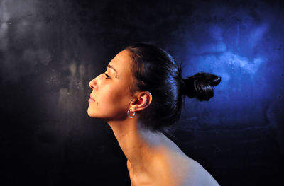 Side view of young woman looking away against wall