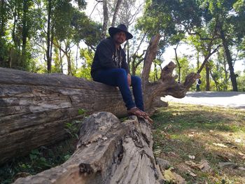 Full length of young man sitting on tree trunk in forest