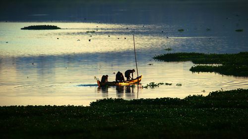 Silhouette people sitting on lake against sky