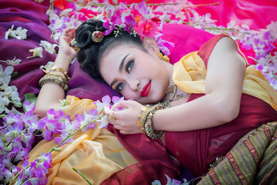 Beautiful young woman wearing traditional clothing while lying on bed with orchids