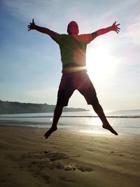 Silhouette of woman jumping on beach at sunset