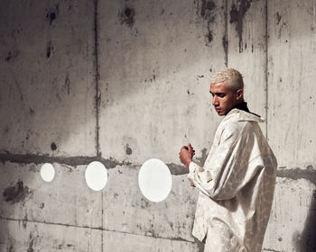 Side view of young man sitting against wall