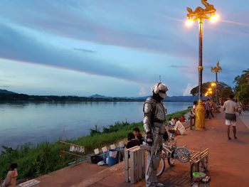 People sitting by lake against cloudy sky