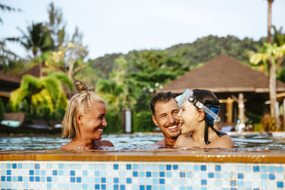 Cheerful girl enjoying with parents in swimming pool at resort during vacation