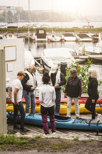 Senior men and women looking at male instructor wearing life jacket while standing by kayaks