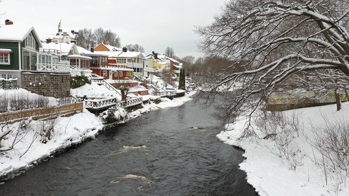 Snow covered houses by canal against buildings