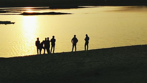 Silhouette people on beach against sky during sunset