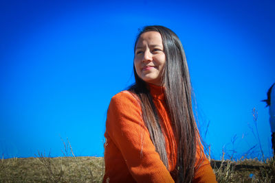 Low angle view of smiling young woman against clear blue sky