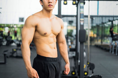 Midsection of shirtless young man standing in gym